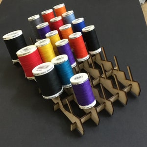 May include: A wooden thread rack with multiple compartments holds spools of colorful thread. The spools are arranged in rows and are labeled with the brand name "G&uuml;termann".