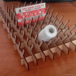 May include: A wooden thread rack with a white spool of thread and a business card for Art-Mari.com.ua. The rack has multiple slots for holding spools of thread.