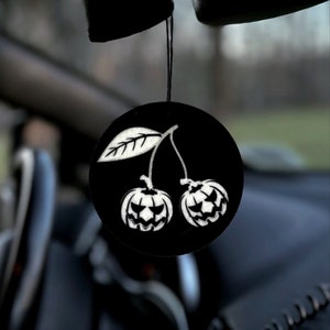May include: Black car air freshener with a white design of two jack-o'-lantern pumpkins with a stem and leaf.