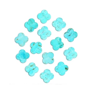 Puede incluir: Una colección de 12 cabujones de turquesa, cada uno con forma de trébol de cuatro hojas. Los cabujones son de color azul claro con inclusiones marrones y doradas.