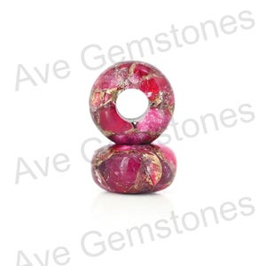 Könnte beinhalten: Zwei runde, polierte Edelsteinperlen. Die Perlen sind eine Mischung aus tiefem Rot und Gold, mit einem Loch in der Mitte. Die Edelsteine haben ein gesprenkeltes Aussehen. Die Perlen sind übereinander gestapelt.