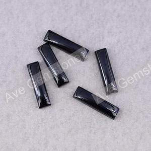May include: Six rectangular, glossy black gemstones are displayed. Each stone has a polished surface and beveled edges. The stones are arranged on a light grey surface, highlighting their dark colour and shape.
