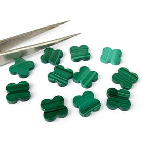 Könnte beinhalten: Eine Sammlung grüner Malachit-Edelstein-Klee-Cabochons. Die Cabochons sind auf einer weißen Oberfläche verstreut.