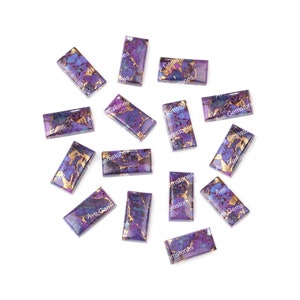 May include: A collection of twelve purple and gold gemstone cabochons. The cabochons are rectangular and have a marbled pattern.