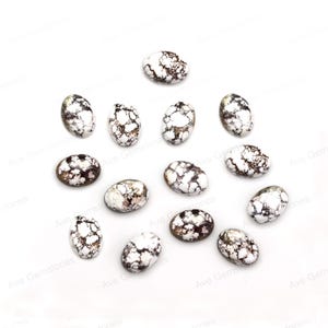 May include: A collection of 15 oval-shaped, white and brown, natural gemstone cabochons. The cabochons are scattered on a white surface.