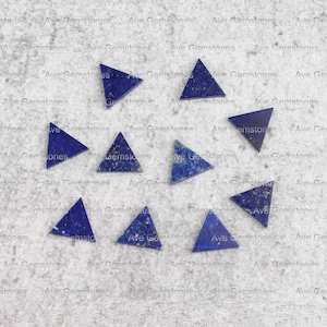 May include: Seven blue triangular lapis lazuli gemstones on a light grey textured surface. The gemstones are various sizes and have a sparkly, iridescent finish.
