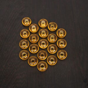 Peut inclure: Un ensemble de 18 anneaux en plastique ambre, disposés en cercle sur une surface brun foncé.