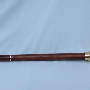 May include: A wooden walking stick with a brass telescope attached to the end. The stick is dark brown with a light brown stripe running down the length of the stick.