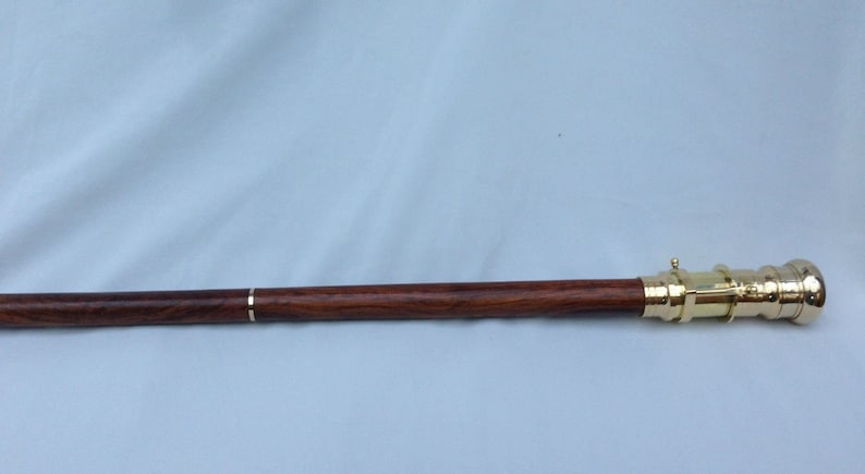 May include: A wooden walking stick with a brass telescope attached to the end. The stick is dark brown with a light brown stripe running down the length of the stick.