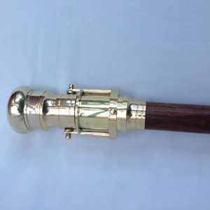 May include: A brass telescope cane with a wooden handle. The telescope is extended and the handle is made of dark wood.