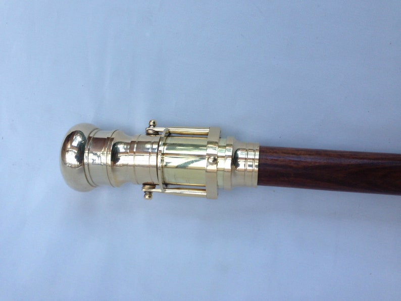 May include: A brass telescope cane with a wooden handle. The telescope is extended and the handle is made of dark wood.