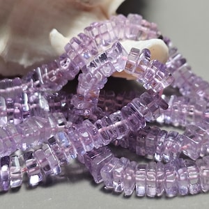 Może przedstawiać: Zbliżenie na sznury jasnofioletowych, kwadratowo ciętych koralików z kamieni szlachetnych. Koraliki są nawleczone, tworząc naszyjnik lub bransoletkę. Kamienie szlachetne są półprzezroczyste, co daje delikatny i elegancki efekt.