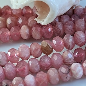 Könnte beinhalten: Eine Strähne aus rosafarbenen und weißen facettierten Edelsteinperlen. Die Perlen sind rund und haben eine glatte, polierte Oberfläche.
