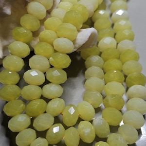 May include: Close-up of strands of faceted, oval-shaped beads in shades of pale yellow and cream. The beads have a polished, reflective surface. The beads are strung together, suggesting jewelry making or craft supplies.