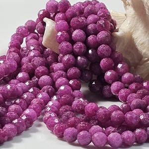 Peut inclure: Gros plan sur des brins de perles de pierres précieuses magenta foncé à facettes. Les perles sont rondes avec de multiples facettes, créant un effet scintillant. Les perles sont enfilées ensemble, formant un collier ou un bracelet.