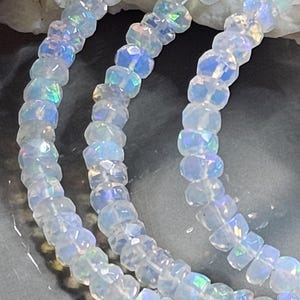 May include: A strand of faceted, translucent white beads with an iridescent finish that reflects blue, green, and pink light. The beads are round and strung together on a thin, clear filament, creating a shimmering, multi-layered appearance.