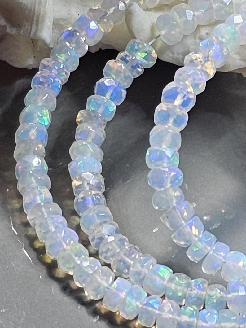 May include: A strand of faceted, translucent white beads with an iridescent finish that reflects blue, green, and pink light. The beads are round and strung together on a thin, clear filament, creating a shimmering, multi-layered appearance.