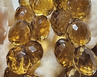 May include: Close-up of faceted, oval-shaped citrine gemstones. The gems are a warm, amber color with multiple facets that catch the light. The citrines are resting on a white, textured surface, creating a contrast in color and texture.