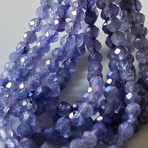 Può includere: Una collana di perline di pietra preziosa blu sfaccettate. Le perline sono piccole e hanno una forma leggermente irregolare. Sono infilate su un filo trasparente.