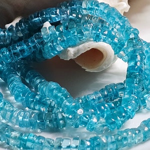 May include: A strand of light blue gemstone beads. The beads are faceted and have a square shape. The beads are strung on a clear thread.