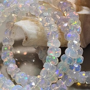 May include: A strand of faceted, translucent white beads with an iridescent finish that displays flashes of green, blue, and orange light. The beads are round and disc-shaped, strung together in a continuous line, reflecting light across their surfaces.