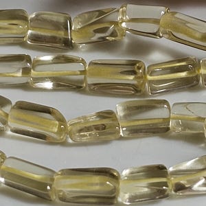 Pode incluir: Close-up de uma fileira de contas retangulares translúcidas com uma faixa amarelo-dourada. As contas são enfiadas, possivelmente para um colar ou pulseira.