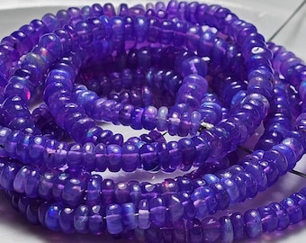 May include: A strand of iridescent purple beads, with a slightly rounded shape. The beads are strung on a clear thread and are arranged in a loose coil.
