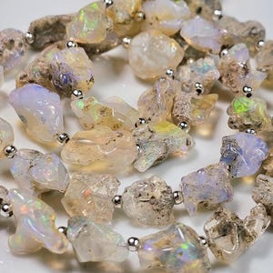 May include: A strand of opal beads, each bead is a unique, irregular shape with a milky white color and flashes of iridescent color. The beads are strung on a silver wire with silver spacer beads.