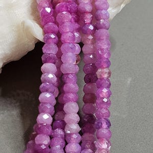Può includere: Primo piano di fili di pietre preziose rosa, rotonde e sfaccettate. Le perle variano in tonalità di rosa e viola, con una finitura lucida. Le pietre sono infilate, ideali per la creazione di gioielli.