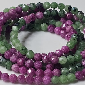 Op de afbeelding: Een opgerolde streng van gefacetteerde ronde kralen met een mix van levendige magenta-roze en gevlekte lichtgroene stenen met af en toe zwarte insluitingen, gerangschikt in een cirkelvormig patroon om de reflecterende textuur te tonen.