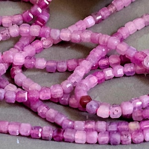 Peut inclure: Gros plan de plusieurs brins de perles de pierres précieuses roses. Les perles sont petites, taillées en carré et varient dans les tons de rose, du clair au magenta foncé. Les perles sont enfilées, créant un affichage texturé et coloré.