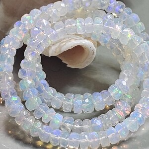 May include: A strand of faceted, translucent white beads with an iridescent finish that reflects flashes of blue, green, and pink light. The small, circular beads are strung together in a loose coil, showcasing their reflective, multi-faceted surfaces.