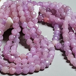 Peut inclure: Gros plan sur plusieurs brins de perles de pierres précieuses violet clair à facettes. Les perles sont enfilées ensemble, créant un effet de superposition. Les perles ont un aspect brillant et poli. L'arrière-plan comprend un coquillage blanc.