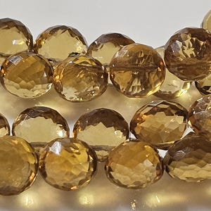 May include: Close-up of faceted, round beads in shades of amber and gold. The beads are strung together, showcasing their intricate cut and reflective surfaces. These gemstone beads are ideal for jewelry making.