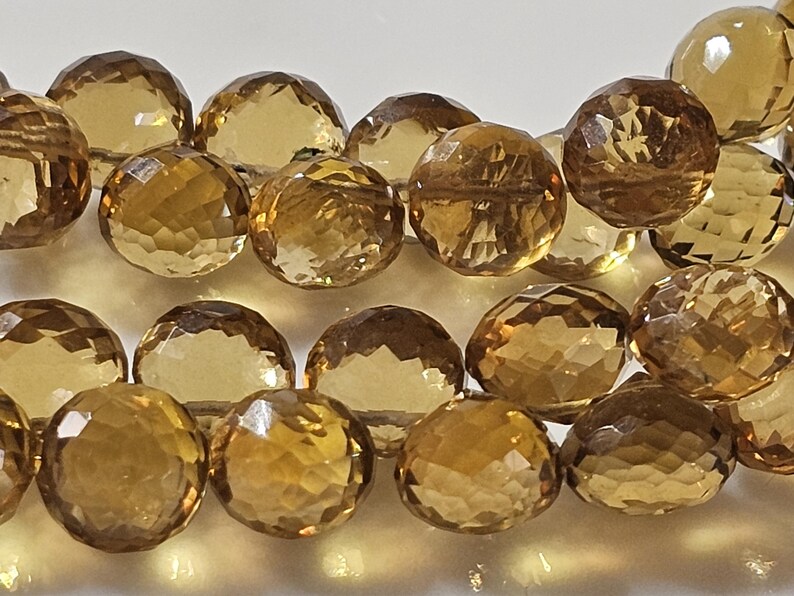 May include: Close-up of faceted, round beads in shades of amber and gold. The beads are strung together, showcasing their intricate cut and reflective surfaces. These gemstone beads are ideal for jewelry making.