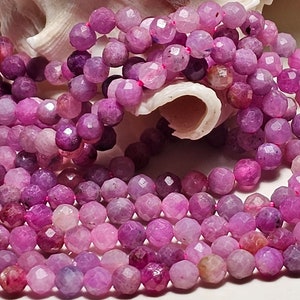 Peut inclure: Gros plan sur plusieurs rangées de perles rondes et facettées, de couleurs rose et violet. Les perles ont une surface polie et réfléchissante. L'image suggère un approvisionnement pour la fabrication de bijoux ou des colliers finis.
