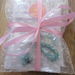 May include: A wrapped package with a light pink ribbon tied in a bow. The package is wrapped in bubble wrap and contains a light blue beaded bracelet. A pink sticker with the words "Thank you" is visible.