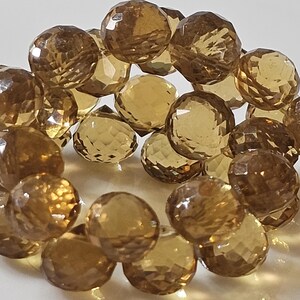 May include: Close-up of a collection of faceted, round, amber-colored gemstone beads. The beads are clustered together, showcasing their multiple facets and translucent quality. The gemstones are a warm, golden brown color.