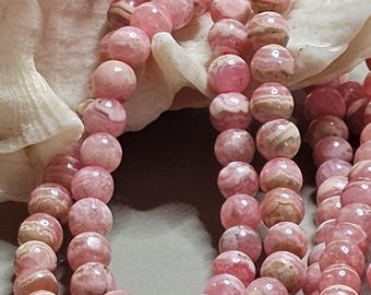 May include: A strand of pink and white striped gemstone beads. The beads are round and have a smooth, polished finish.