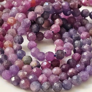 Può includere: Un filo di perline di pietre preziose sfaccettate in tonalità di viola, rosa e lavanda. Le perline sono rotonde e hanno una forma leggermente irregolare.