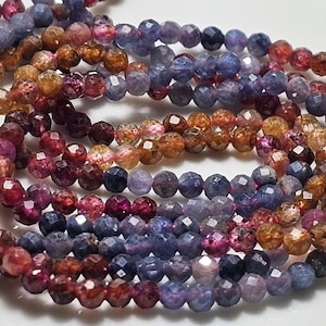 Peut inclure: Un brin de perles de pierres précieuses facettées dans des tons de bleu, rose et marron. Les perles sont petites et rondes, et elles sont enfilées sur un fil transparent.