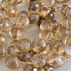 May include: Close-up of a collection of faceted, round gemstones in shades of amber and brown. The gemstones are scattered, showcasing their multiple facets and translucent quality. Ideal for jewelry making.