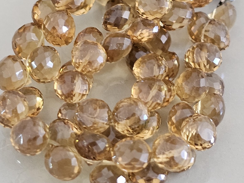 May include: Close-up of a collection of faceted, round gemstones in shades of amber and brown. The gemstones are scattered, showcasing their multiple facets and translucent quality. Ideal for jewelry making.
