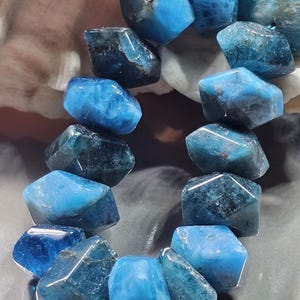 Op de afbeelding: Een streng van gefacetteerde, onregelmatige blauwe apatietkralen. De stenen vertonen een scala aan diep marineblauwe tot helder cyaan tinten met natuurlijke insluitingen en een gepolijst, reflecterend oppervlak met diverse hoekige vlakken.