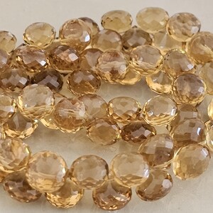 May include: A collection of faceted, round gemstones in shades of amber and brown. The beads have a polished, reflective surface, and are strung together. The gemstones vary in color, with some being lighter and others darker.