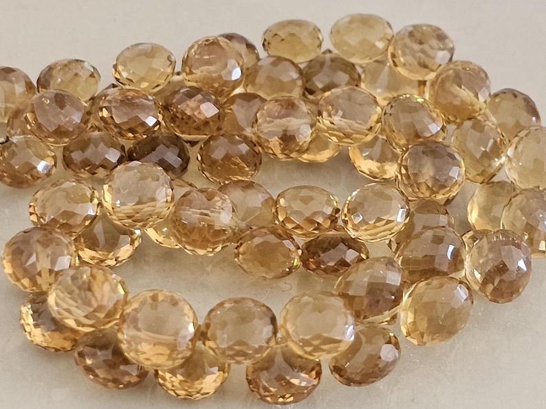May include: A collection of faceted, round gemstones in shades of amber and brown. The beads have a polished, reflective surface, and are strung together. The gemstones vary in color, with some being lighter and others darker.