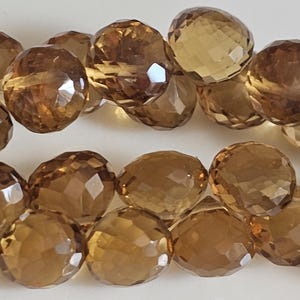 May include: Close-up of faceted, round, amber-colored gemstone beads. The beads have a polished, reflective surface and are strung together. The gemstones are a warm, earthy tone, and the facets catch the light.