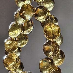 May include: A strand of faceted, golden-yellow gemstone beads. The beads are round with multiple facets, reflecting light. The gemstones are strung together, creating a necklace or bracelet.