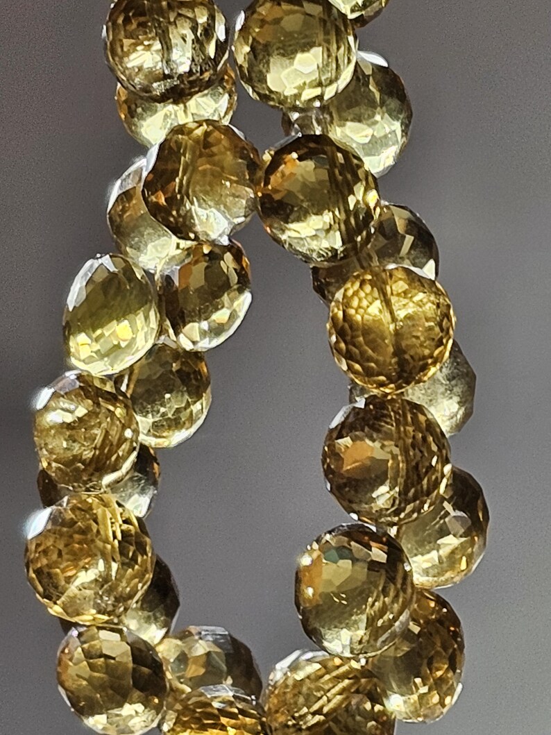 May include: A strand of faceted, golden-yellow gemstone beads. The beads are round with multiple facets, reflecting light. The gemstones are strung together, creating a necklace or bracelet.