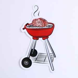 May include: A red grill with a brain on top of it. The grill has a black grate and a black handle. There is smoke coming from the top of the grill.